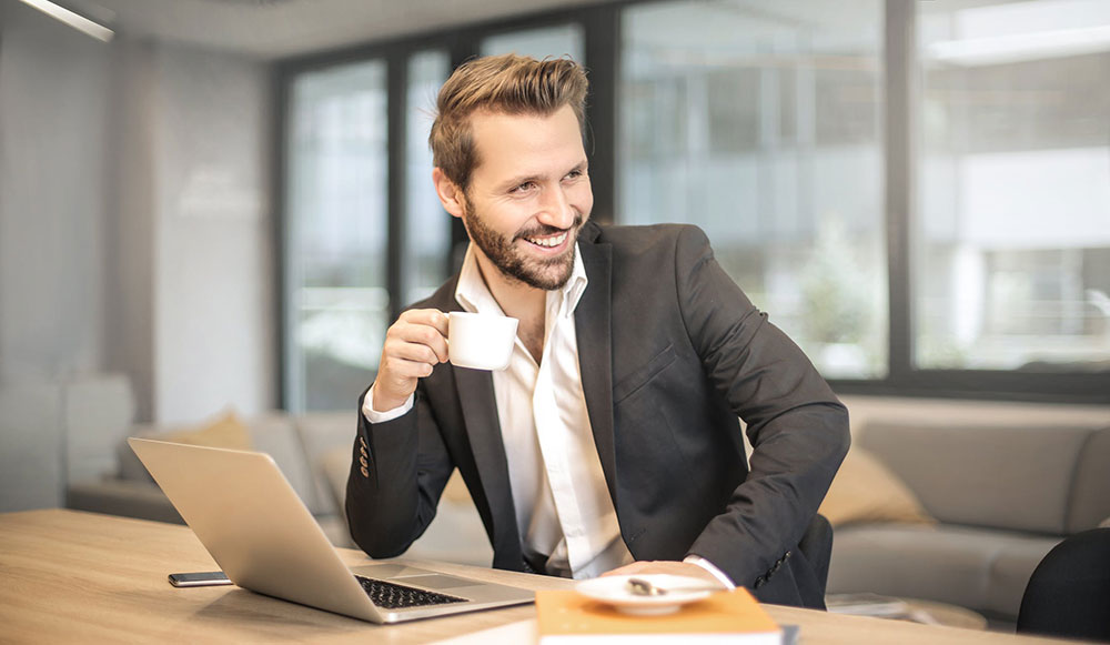 Man drinking coffee in front of laptop confidently