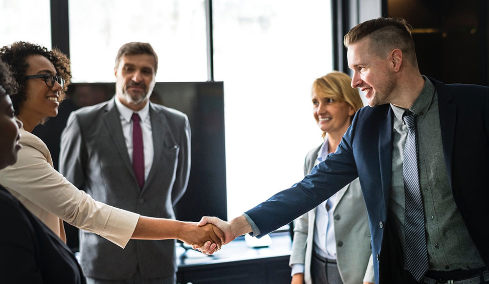 Man and woman shaking hands in front of coworkers