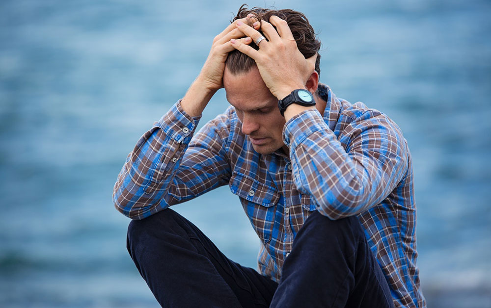 White man with plaid shirt sitting stressed out by ocean