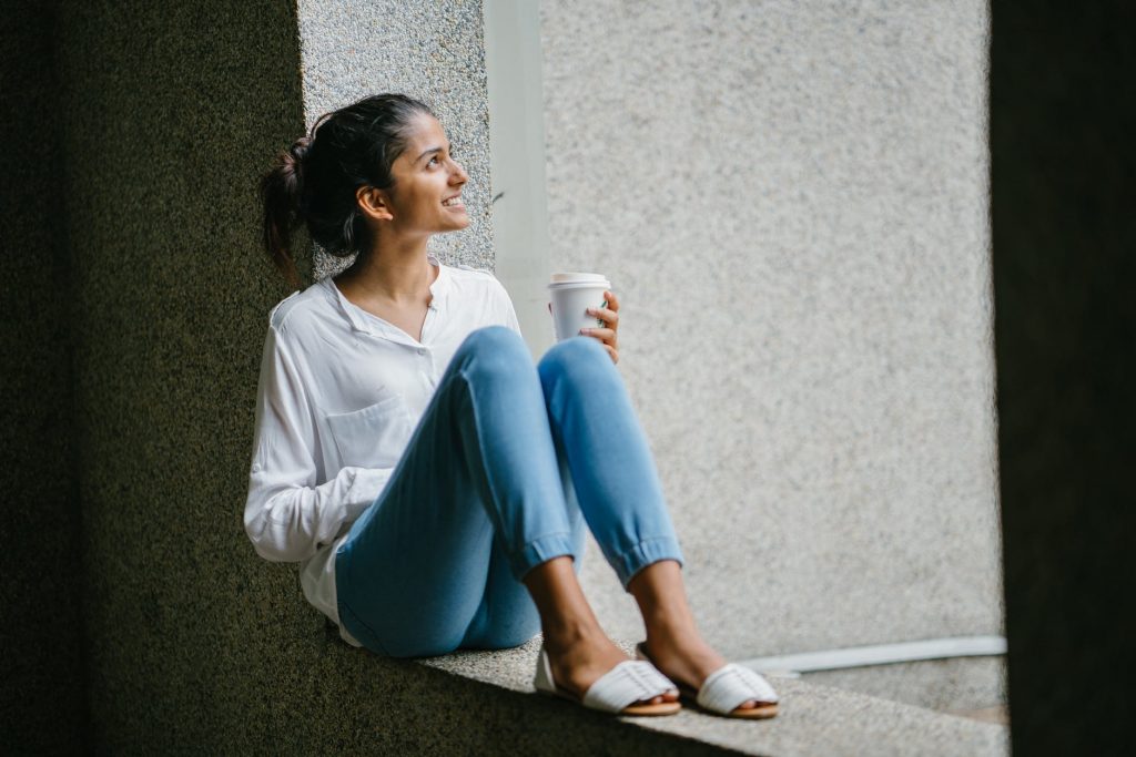Young woman taking a break with her coffee while sitting on window ledge