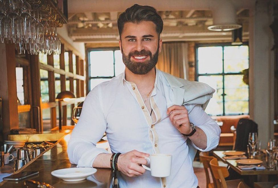 man smiling holding a coat and cup