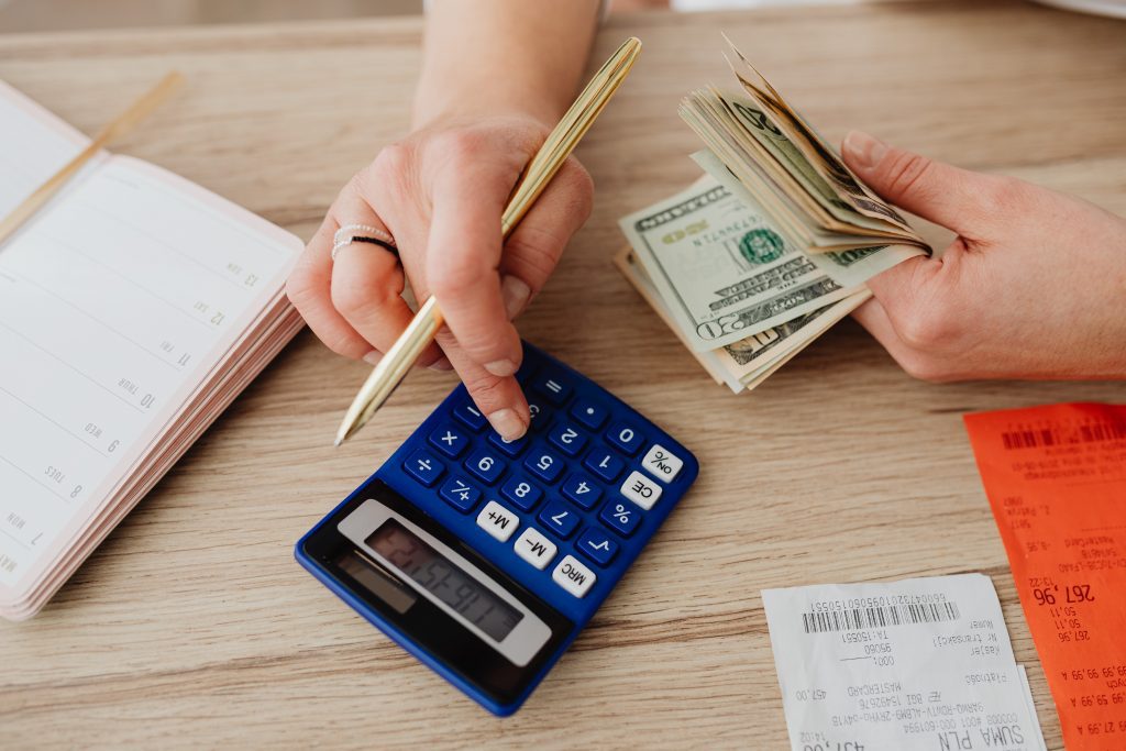 Person holding a wad of cash and a pen typing on a calculator