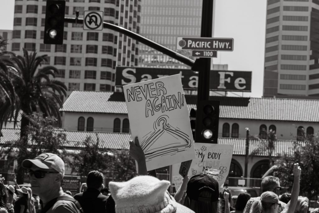 A protestor carrying a sign that reads "never again" with a drawing of a coat hanger