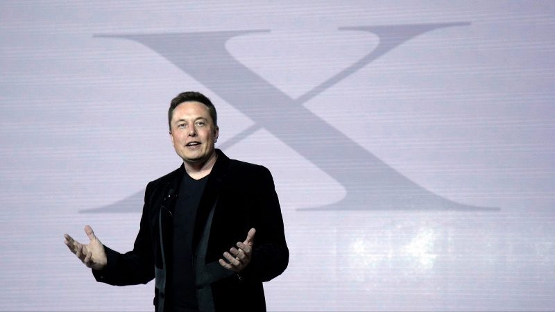Elon Musk standing in front of a large letter X