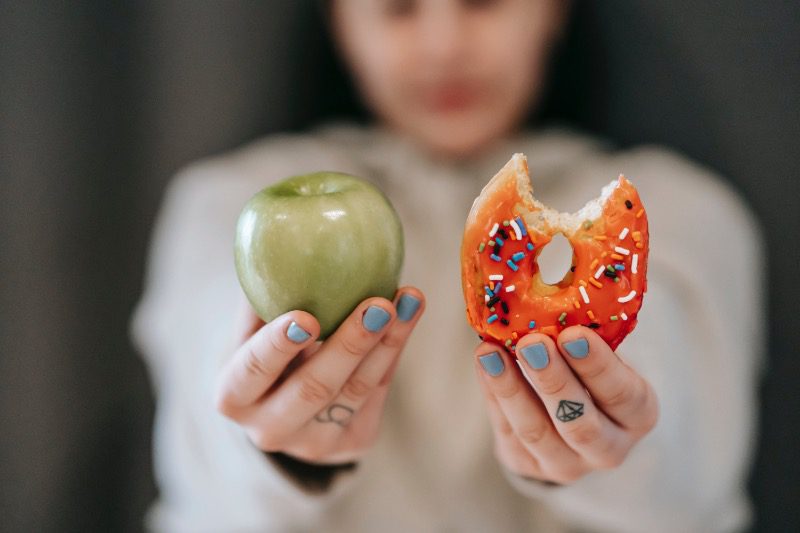 A photo of a person holding up an apple and a donut, representing the choice between Penji, Manypixels, and No Limit Creatives