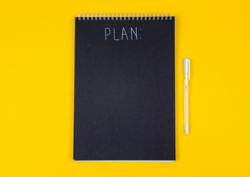 A notebook reading "PLAN" on a yellow background